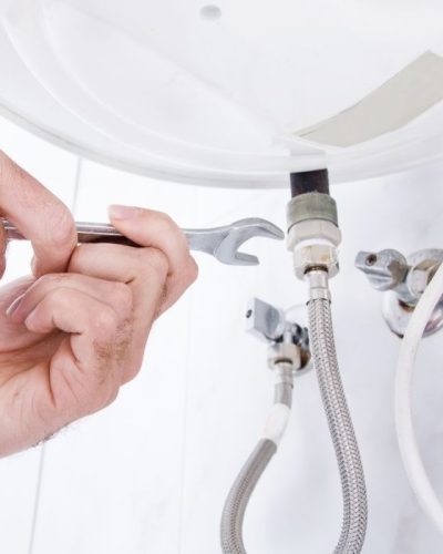 Person fixing under-sink plumbing with wrench.